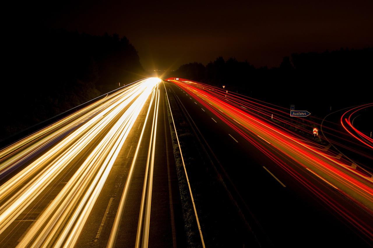 Nachtaufnahme einer Autobahn mit Langezitbelichtung, wo die vorbeifahrenden Fahrzeuge nur als weiße und rote Lichtstreifen zu erkennen sind.