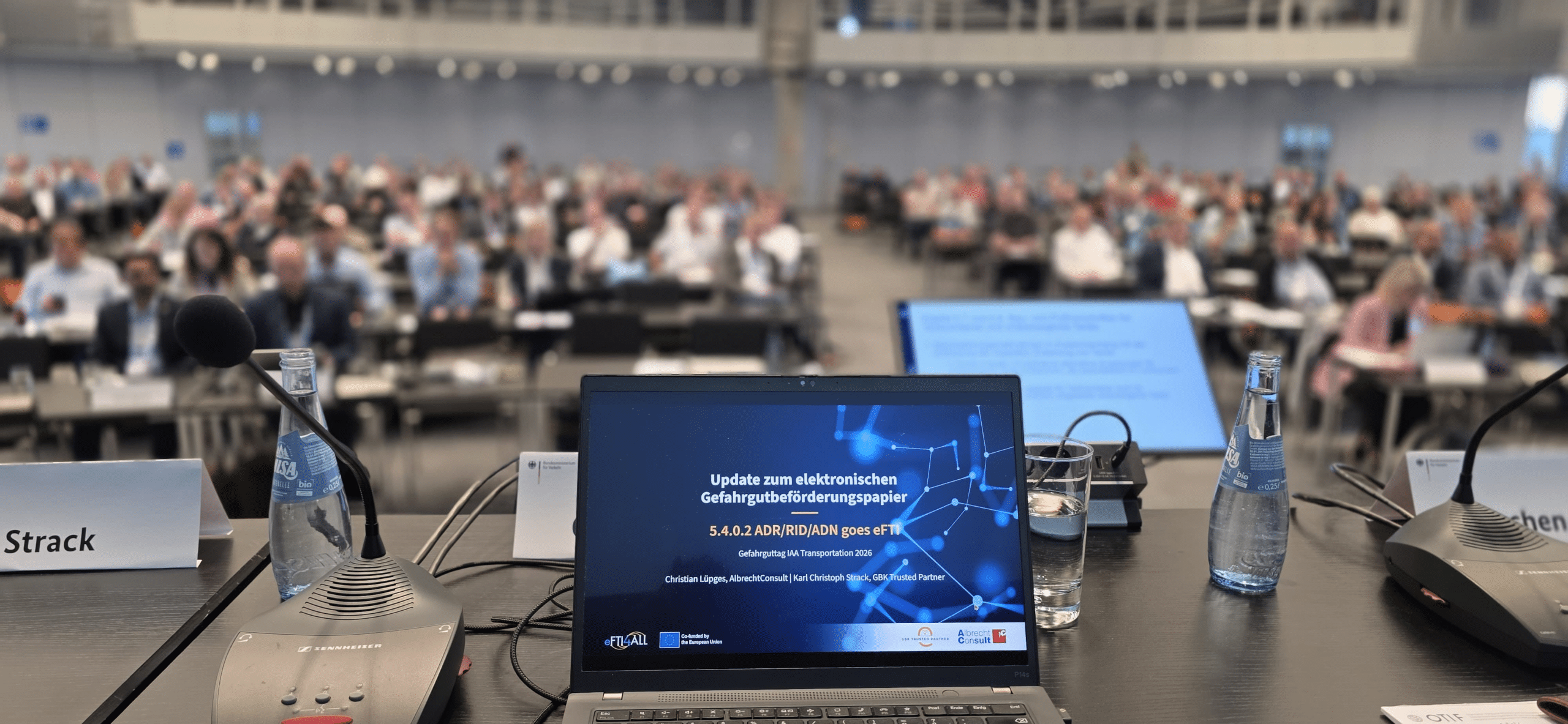 View from the panel table into the conference hall: a laptop displays the title slide of the eFTI presentation, with the audience in the background.